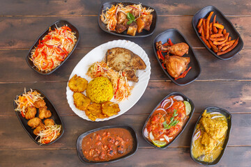 Variété de plats antillais et créoles (accras de morue, colombo de poulet, fricassée de chatrou, court-bouillon de poisson, griot de porc, pikliz, riz Djon Djon, bananes pesées) sur une table en bois 