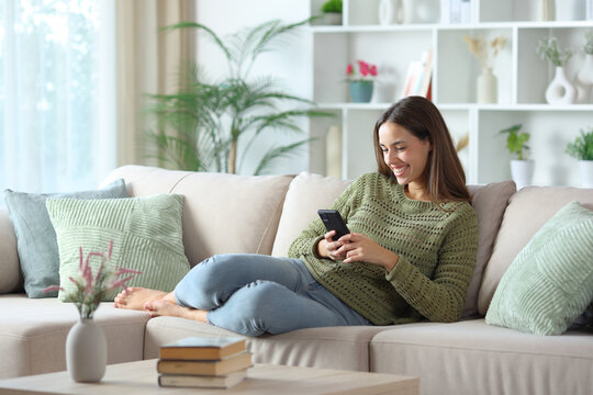 Happy woman in green using smart phone on a couch