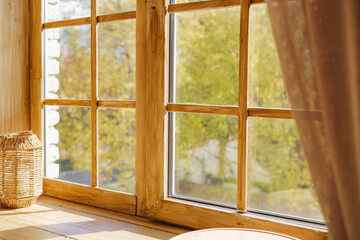 Fototapeta premium Warm sunlight through wooden window panes showing autumn trees and brown curtain detail