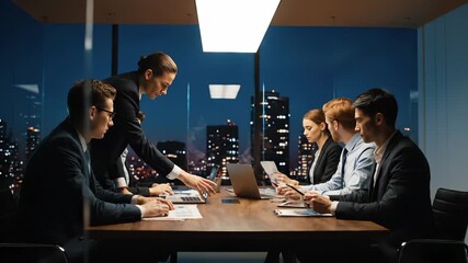 Business meeting in conference room. Team and executive discuss strategy around laptop. Colleague reviews document and presentation. Boardroom with night city skyline. Office team focused on result.