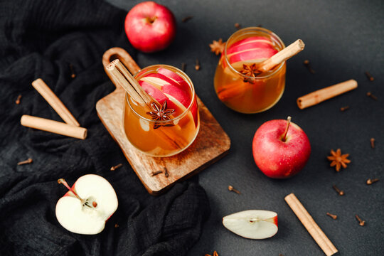 Warm apple drink with cinnamon sticks and star anise, garnished with fresh red apples.