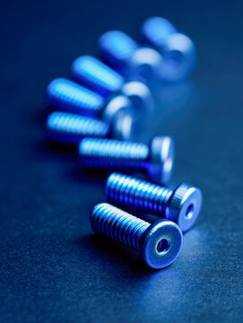 Metallic screws with hex socket heads arranged in a diagonal line on a dark surface featuring blue lighting and shallow depth of field for industrial concept visuals