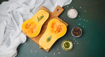 Butternut squash halved on wood board with herbs, salt, peppercorns, and oil