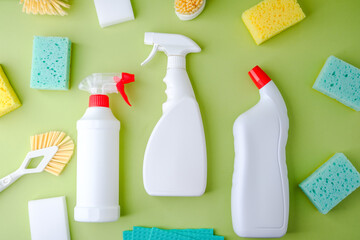 White cleaning bottles and colorful sponges arranged on a light green background with brushes