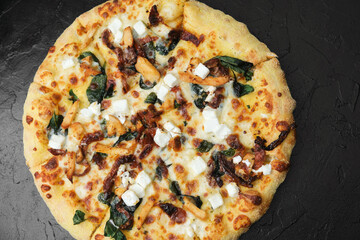 Gourmet pizza with spinach feta chicken and sun dried tomatoes served on black textured background