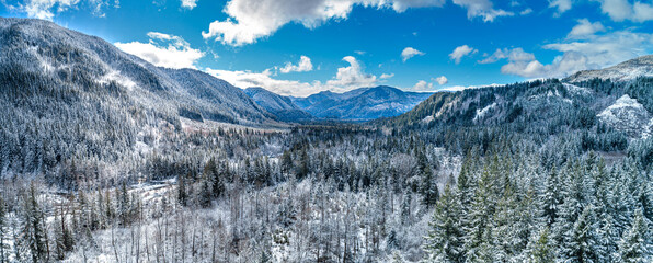 Aerial view of snow-laden trees blanketing the landscape of the valley between the mountains under the bright blue sky, Mt Hood, Oregon, United States.