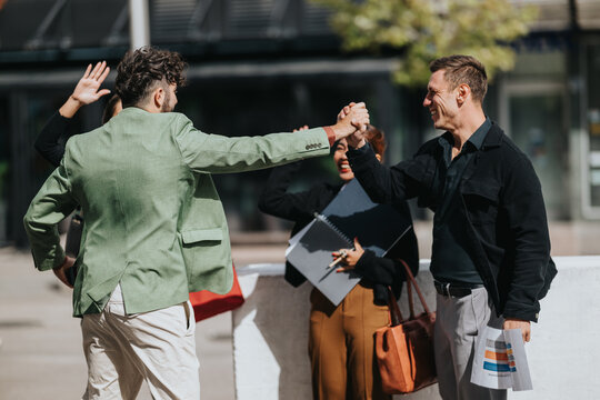 A group of colleagues in casual business attire share a high-five on a sunny outdoor day, signaling success, collaboration, and camaraderie after a productive meeting.