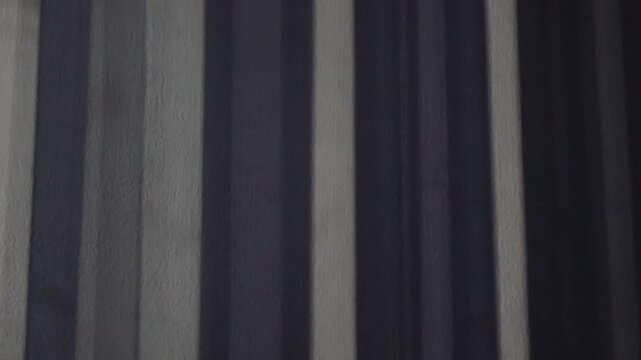 Una toma de cerca de una persiana en movimiento de una ventana reflejada en la pared de una habitaci&oacute;n  con una luz artificial en la noche