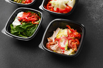 Mixed salads with fresh vegetables meat cheese and greens in black containers for restaurant delivery or meal prep concept