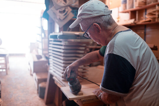 Senior craftsman meticulously sanding wooden piece in workshop