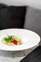 gourmet crab or seafood salad tartare with red caviar, avocado, and microgreens served on a modern white rimmed plate in a restaurant setting.