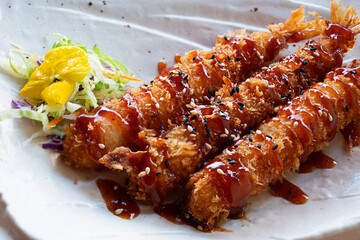 Close-up of traditional Japanese dish shrimp tempura, deep-fried, served on minimalist white plate.