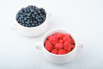 Blueberries and raspberries  cups on white for colorful snack or paired fruit concept