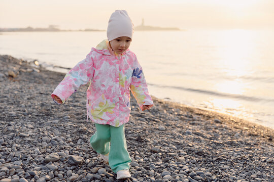 Child in warm clothes playing on a rocky beach at sunset