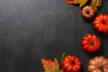 A festive autumn flat lay with pumpkins and leaves on a black concrete background. Thanksgiving greeting card design. Autumn fall
