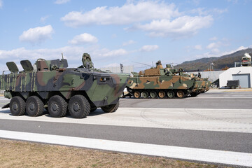 Obraz premium Two military armored vehicles, one wheeled and one tracked, are displayed outdoors on a sunny day, showcasing modern defense technology and tactical mobility in a training area.