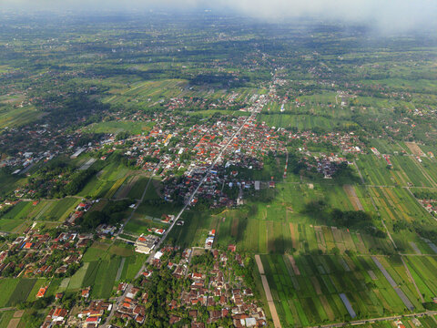 Aerial view of a vibrant patchwork of rice paddies and village settlements under the vast Indonesian sky, Klaten Regency, Central Java, Indonesia.