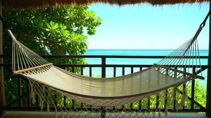 A hammock hangs on a balcony overlooking the turquoise ocean on a sunny day