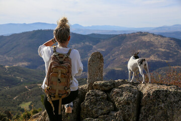 Blonde woman with a bun looking at the mountains after walking along the paths accompanied by her dog