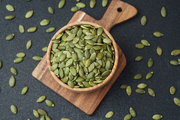 Pumpkin seeds in wooden bowl on cutting board with black background