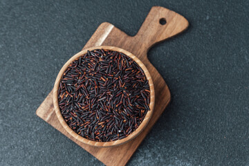Black rice in wooden bowl on cutting board over dark background