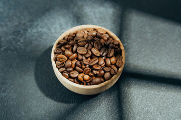 Coffee beans in wooden bowl with shadow on dark background
