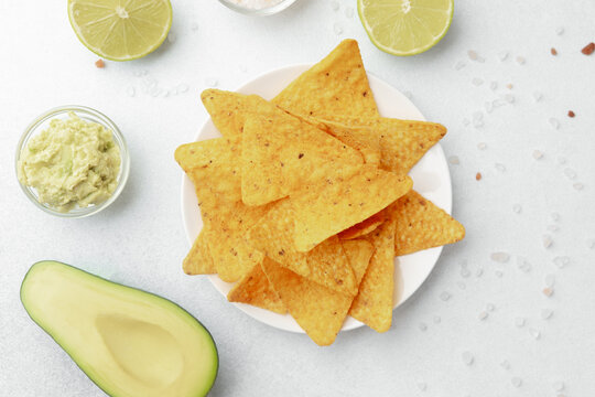 Guacamole, lime, avocado and nacho chips on white background with salt