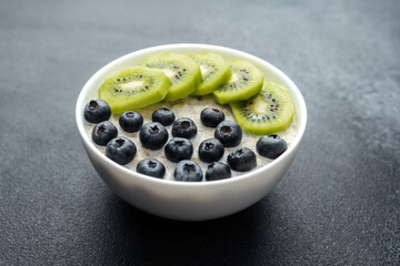 Oatmeal bowl with kiwi and blueberries with assorted fruit on black table