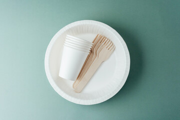 Disposable white paper cups and wooden forks on plate with green background