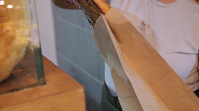 Close-up of a baker putting freshly baked bread in a paper disposable bag. The baker packs the bread, which has just been taken out of the oven, into environmentally friendly paper bags. Tandoor bread
