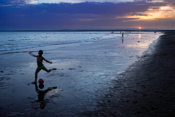Child plays football at sunset on wet sands of Ayamonte beach