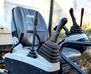 Detailed close-up shot of the interior cabin and controls of a Komatsu mini-excavator or compact construction machine, featuring the seat, joystick, and control levers. © YuliiaKettu