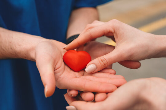 Hands exchanging a red heart symbolizing love and care in a warm moment