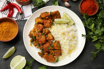 Delicious chicken tikka masala with rice, parsley, lime and spices on dark textured table, flat lay