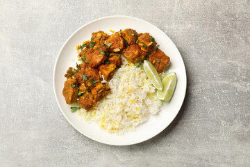 Delicious chicken tikka masala with rice, parsley and lime on grey textured table, top view