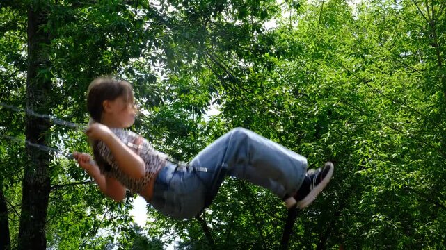 Teenage girl nestled on swing finds solace in the empty park, savours moment of unhurried day. Summer vacations, brightly lit by sunlight and set against a backdrop of lush green trees and sky.