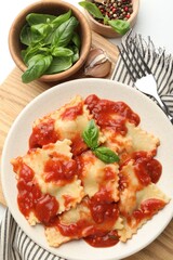 Delicious ravioli with tomato sauce and basil served on white wooden table, flat lay
