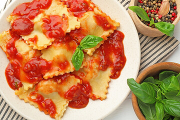 Delicious ravioli with tomato sauce, basil and spices on white wooden table, flat lay