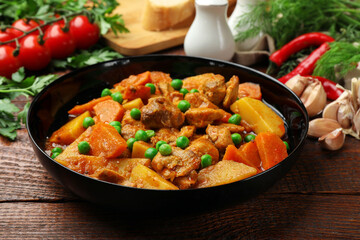 Delicious cooked stew and fresh ingredients on wooden table, closeup