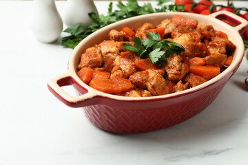 Delicious cooked stew in baking dish and fresh ingredients on white marble table, closeup