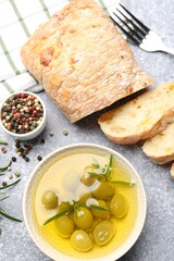 Fresh cut ciabatta, oil, olives and peppercorns on grey textured table, flat lay