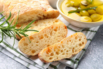 Fresh cut ciabatta, oil, olives and rosemary on grey textured table, closeup