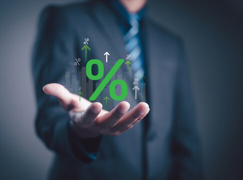 Businessman holding floating green percentage symbol with upward arrows, representing growth, interest rate, profit, and financial success in investment and business performance analytics.