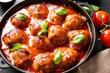 Meatballs in tomato sauce in iron plate on black background.