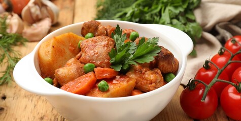Delicious cooked stew in bowl and ingredients on wooden table, closeup