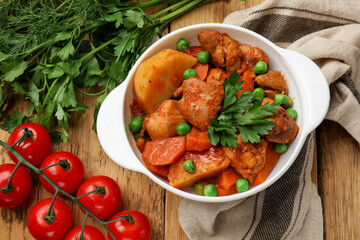 Delicious cooked stew in bowl and ingredients on wooden table, flat lay