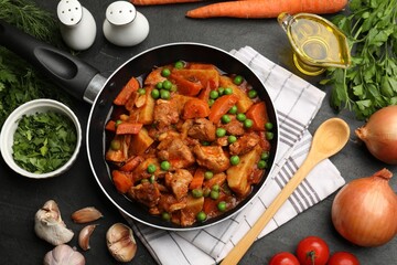 Delicious cooked stew in frying pan and ingredients on black table, flat lay