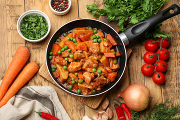Delicious cooked stew in frying pan and ingredients on wooden table, flat lay