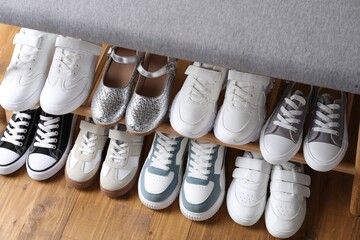 Storage bench with different kid's shoes on wooden floor, above view