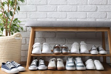 Different kid's shoes on storage bench and houseplant near white brick wall indoors